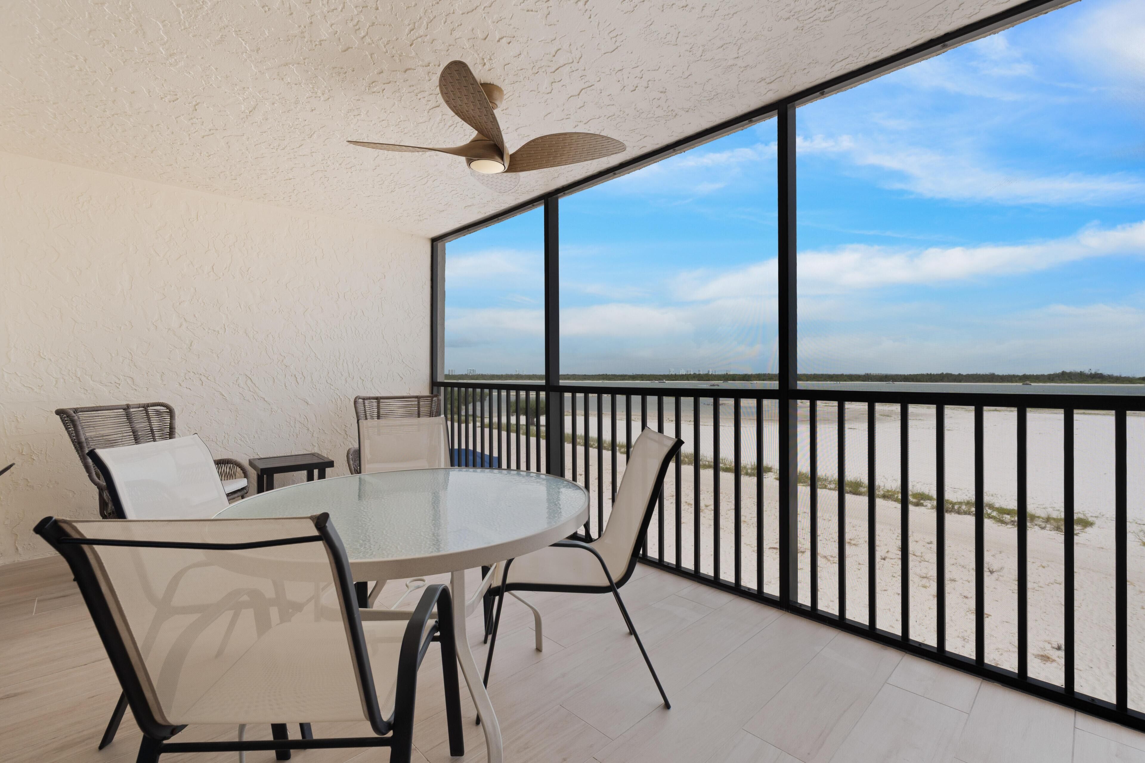 Un balcon avec une table ronde en verre, des chaises et un ventilateur de plafond.