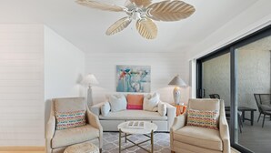 Ein modernes Wohnzimmer mit einer Couch, zwei Sesseln, einem Couchtisch, einem gemusterten Teppich und einem Deckenventilator.