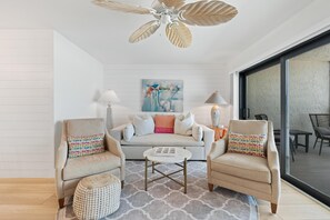 A modern living room with a sofa, two armchairs, a coffee table, a patterned rug, and a ceiling fan. - Carlos Pointe #231 Beach Bum Getaway (Fort Myers Beach)