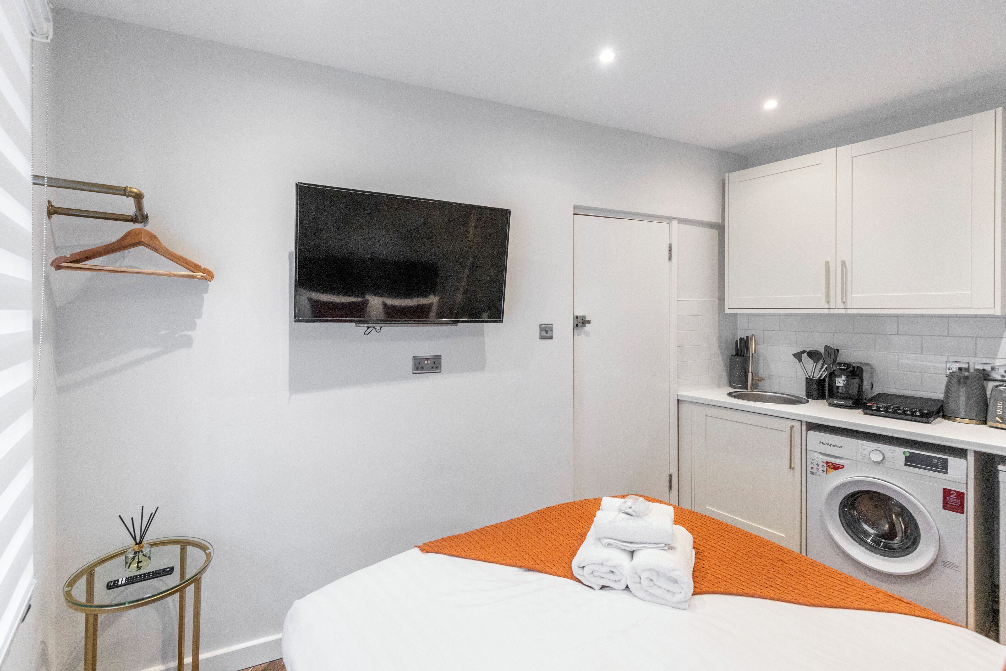 A hotel room with a bed, a television, a washing machine, and a small table with a bottle of water.