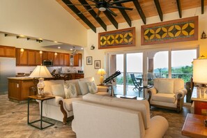 A spacious living area with a kitchen, a balcony with a view, and a ceiling fan. - Cay Syrah! 4 bedroom home! Solar/battery backup! (Cruz Bay)
