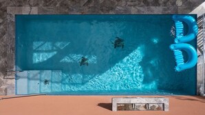 A rectangular swimming pool with clear blue water, a blue floating toothbrush, and a stone wall in the background. - Cay Syrah! 4 bedroom home! Solar/battery backup! (Cruz Bay)