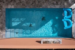 A rectangular swimming pool with clear blue water, a blue floating toothbrush, and a stone wall in the background. - Cay Syrah! 4 bedroom home! Solar/battery backup! (Cruz Bay)
