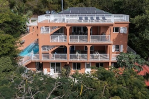 A multi-story building with balconies, a swimming pool, and surrounding greenery. - Cay Syrah! 4 bedroom home! Solar/battery backup! (Cruz Bay)