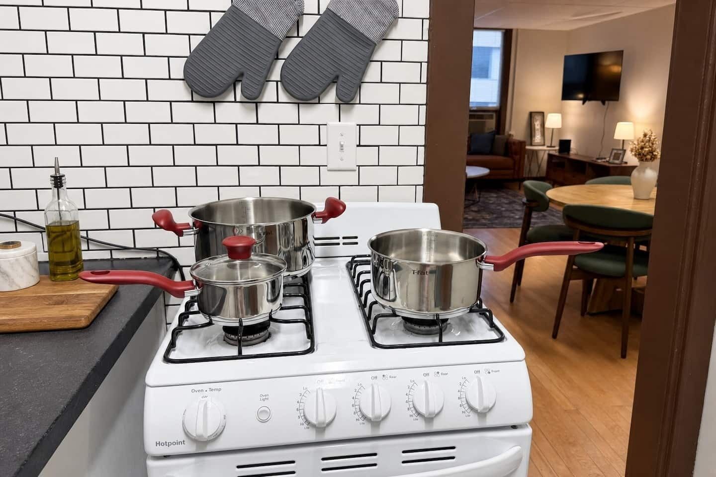 A kitchen with a gas stove, three pots, a bottle of oil, and a marble cutting board.
