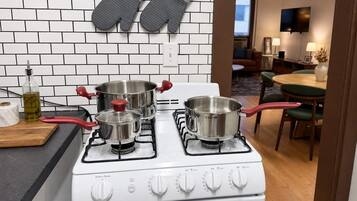 A kitchen with a gas stove, three pots, a bottle of oil, and a marble cutting board.