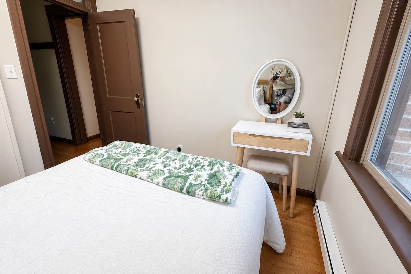 Ein Schlafzimmer mit Bett, Nachttisch, Spiegel und Fenster.