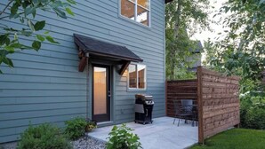 Et hus med mørkeblå facade, en fordør, en lille terrasse med grill og et træhegn.