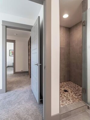 A walk-in shower with a tiled floor, a door leading to a hallway, and a ceiling light. - Bozeman Home with Private Fishing Access (Bozeman)