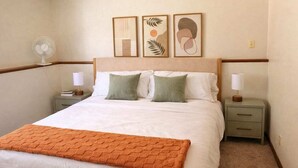 A neatly made bed with a white and orange blanket, two bedside tables with lamps, and three framed artworks on the wall. - Family-friendly duplex near Fargodome, kings+bunk (Fargo)