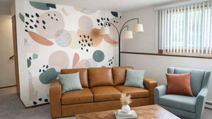 A living room with a brown leather sofa, a blue armchair, a wooden coffee table, and abstract wall art.