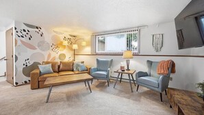 A living room with a sofa, two armchairs, a coffee table, a lamp, and a TV mounted on the wall.