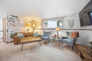 Ett vardagsrum med en soffa, två fåtöljer, ett soffbord, en lampa och en tv som är monterad på väggen.
