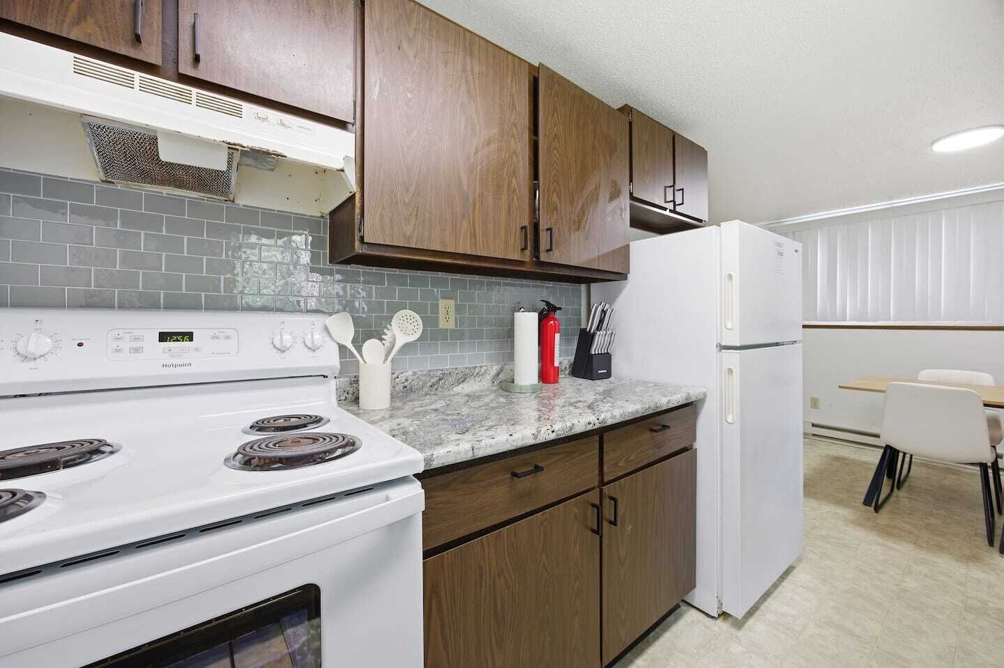Una cocina con armarios de madera, una estufa blanca, un refrigerador y un comedor con mesa y sillas.