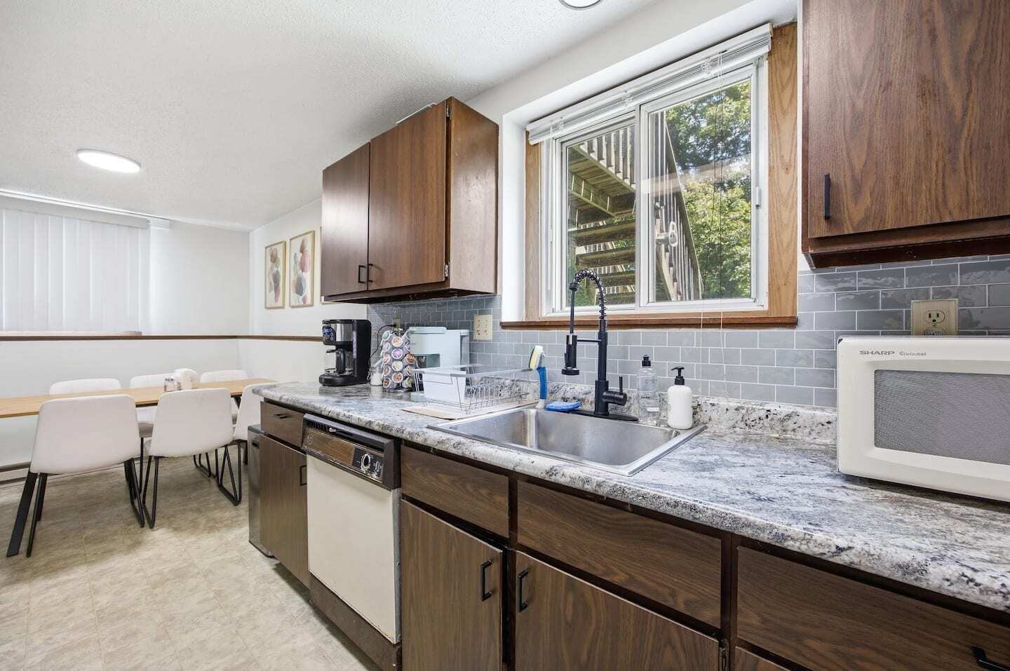 A modern kitchen with a built-in dishwasher, a large window, and a dining area with a table and chairs.