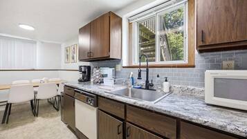 A modern kitchen with a built-in dishwasher, a large window, and a dining area with a table and chairs.