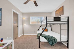 Ein Schlafzimmer mit Etagenbetten, Deckenventilator, Schreibtisch und einem Fenster mit Jalousien.