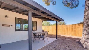 A covered patio with a table and chairs, a wooden fence, and a tree. - Midtown Cozy Getaway! (Tucson)