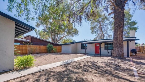 A modern house with a covered patio, a red door, and a large tree providing shade. - Midtown Cozy Getaway! (Tucson)