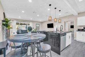 A modern kitchen with a central island, pendant lighting, and a dining area with round tables. - Midtown Cozy Getaway! (Tucson)