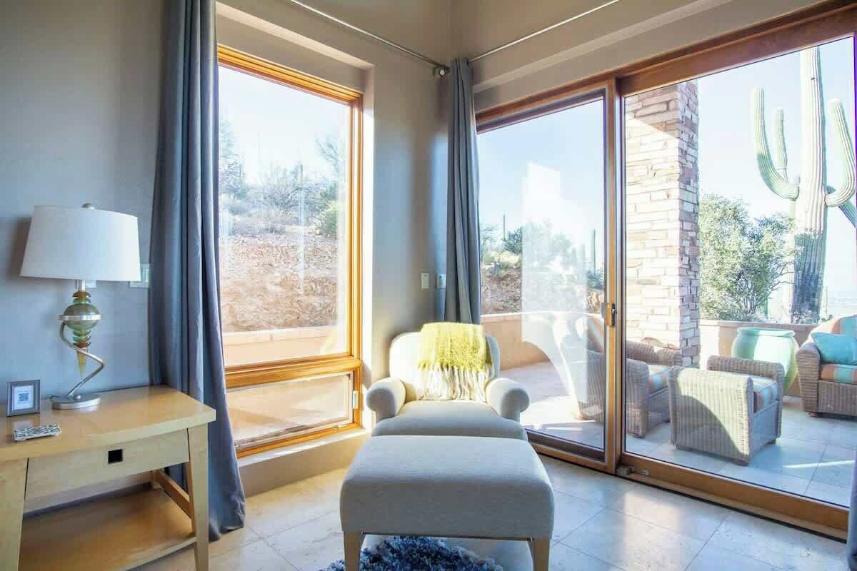Een kamer met een bureau, een stoel, een bank en een grote glazen schuifdeur naar een buitenruimte met cactussen.