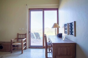 A room with a wooden desk, two chairs, a lamp, and a sliding glass door leading to a patio with chairs. - Exquisite Starr Pass Desert Haven with Pool (Tucson)