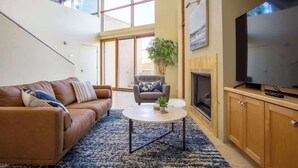 A modern living room with a sofa, armchair, coffee table, TV, fireplace, and a staircase leading to an upper level. - Exquisite Starr Pass Desert Haven with Pool (Tucson)