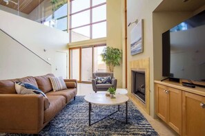 A modern living room with a sofa, armchair, coffee table, TV, fireplace, and a staircase leading to an upper level. - Exquisite Starr Pass Desert Haven with Pool (Tucson)