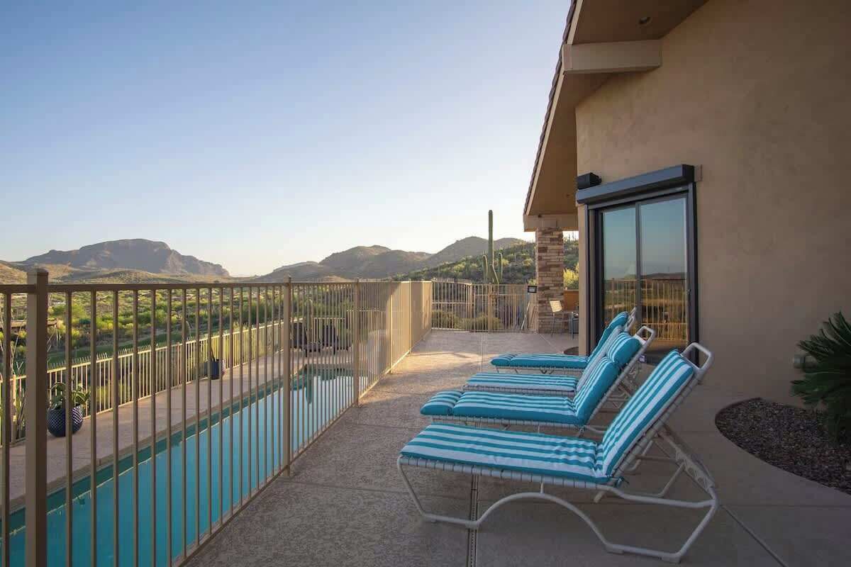 A balcony with a pool, lounge chairs, and a view of mountains.