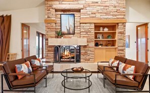 A living room with a stone fireplace, two sofas with patterned cushions, a coffee table, and a bookshelf. - Exquisite Starr Pass Desert Haven with Pool (Tucson)