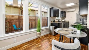 A kitchen with white cabinets, a dining area with a round table, and a view of a backyard with a wooden fence and chairs. - Historic Studio near 4th Ave and U of A (Tucson)