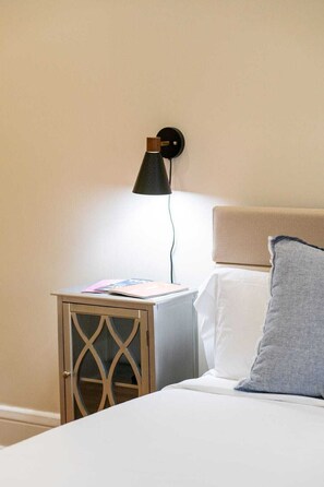 A bed with a headboard, a bedside table with a lamp, and a nightstand with a glass door. - Historic Studio near 4th Ave and U of A (Tucson)