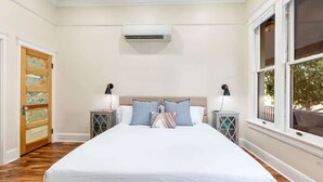 A bedroom with a large bed, two bedside tables, an air conditioning unit, and a window with a view. - Historic Studio near 4th Ave and U of A (Tucson)