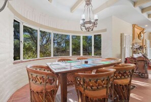 A dining area with a large table, wicker chairs, and a view of trees through large windows. - Southwest Gem-Pool & Mountain Views (Tucson)