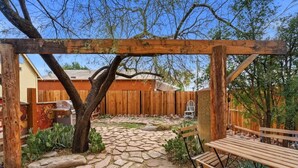 A stone patio with a wooden pergola, a bench, and a wooden fence in the background. - Walkable Barrio Charm (Tucson)