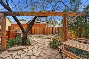 Eine Steinterrasse mit einer Holzpergola, einer Bank und einem Holzzaun im Hintergrund.