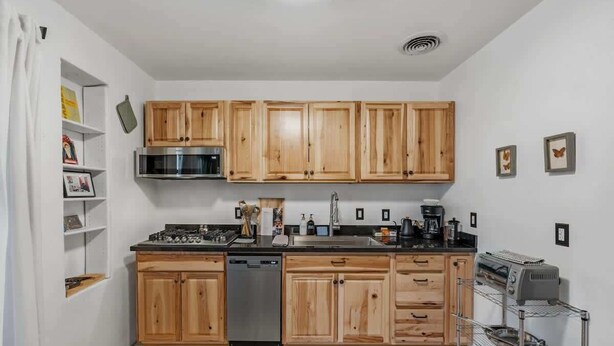A compact kitchen with wooden cabinets, a dishwasher, a microwave, and a coffee maker. - Walkable Barrio Charm (Tucson)