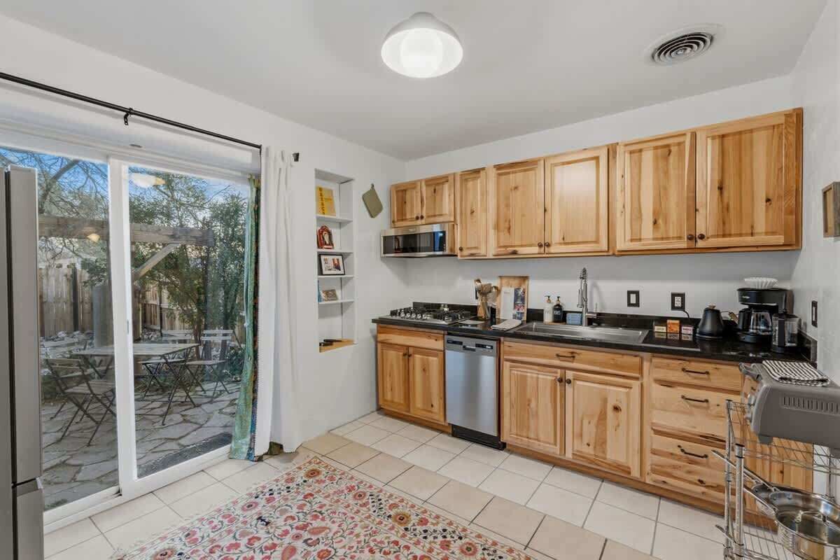 Une cuisine dotée de meubles en bois, d’un lave-vaisselle, d’une cuisinière et d’une grande porte-fenêtre coulissante donnant sur un patio extérieur.