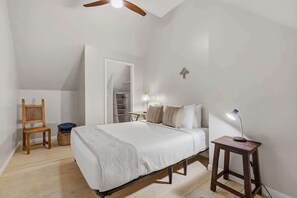 Ein Schlafzimmer mit Bett, Sessel, Nachttisch mit Lampe, Kleiderschrank und Deckenventilator.