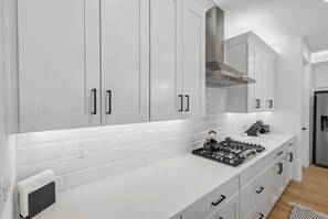A modern kitchen with white cabinets, a stainless steel range hood, and a gas stove. - Exceptional Desert Escape w/ Pool and Spa (Marana)