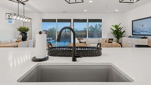A modern kitchen with a central island, a dining area with a view of a pool, and a living room with a TV. - Exceptional Desert Escape w/ Pool and Spa (Marana)