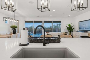 A modern kitchen with a central island, a dining area with a view of a pool, and a living room with a TV. - Exceptional Desert Escape w/ Pool and Spa (Marana)