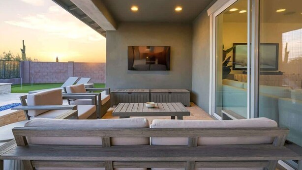A covered outdoor seating area with a pool, lounge chairs, and a large window. - Exceptional Desert Escape w/ Pool and Spa (Marana)