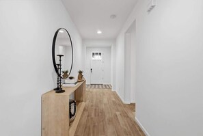 Een gang met een houten console tafel, een spiegel en een deur aan het einde.