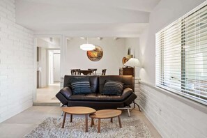 A modern living room with a leather sofa, two wooden side tables, a round coffee table, a hanging light fixture, and a window with blinds. - Spacious Family Getaway-Pet Friendly! (Tucson)