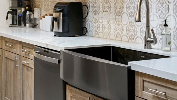 Een keuken met houten kastjes, een roestvrijstalen vaatwasser, een koffiezetapparaat en een betegelde spatwand.