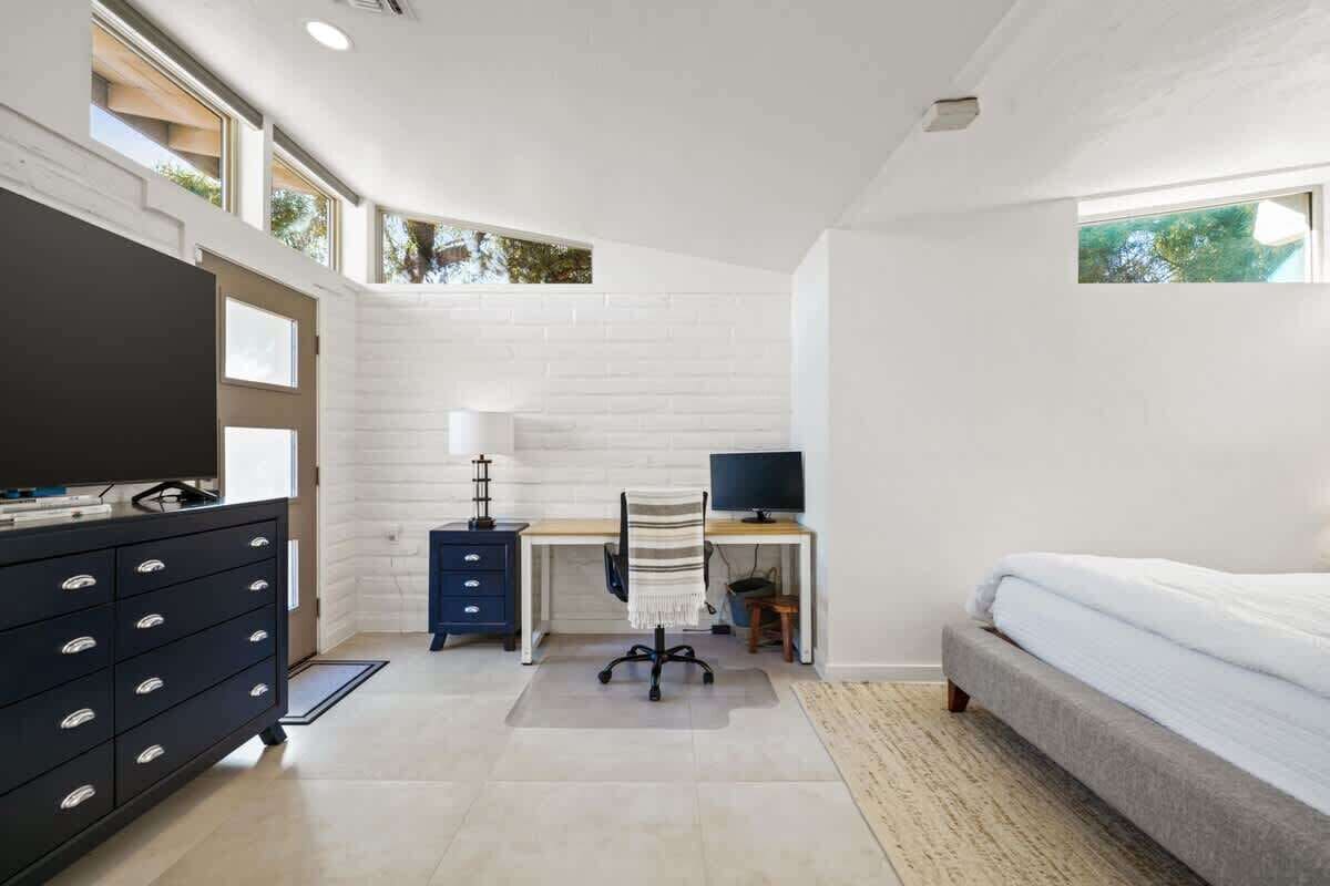 A bedroom with a bed, a desk, a chair, a dresser, and a television.