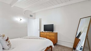 Een slaapkamer met een bed, een dressoir, een televisie en een spiegel.