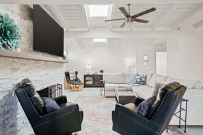 A modern living room with a fireplace, a flat-screen TV, a ceiling fan, and a sofa. - Spacious Family Getaway-Pet Friendly! (Tucson)