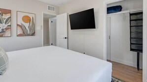 Un dormitorio con cama, televisor de pantalla plana, armario y decoración abstracta en la pared.